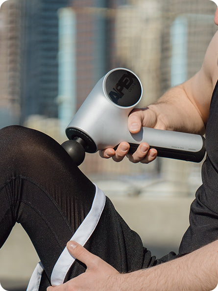 A young man using the opove Apex Massage Gun, a handheld premium percussive therapy device with an ergonomic 45º holding angle, to relieve muscle tension in his leg.