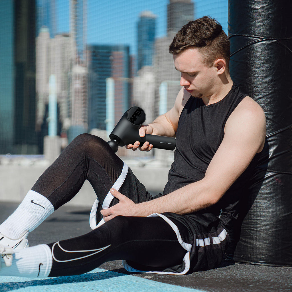 A young man using the Opove Apex Massage Gun, a premium percussive therapy device with an ergonomic 45º holding angle, to relieve muscle tension in his leg.
