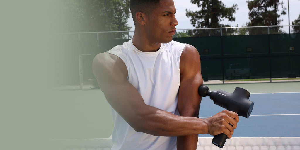 An athlete massages his arms with the Opove M3 Pro massage gun after a tennis match.