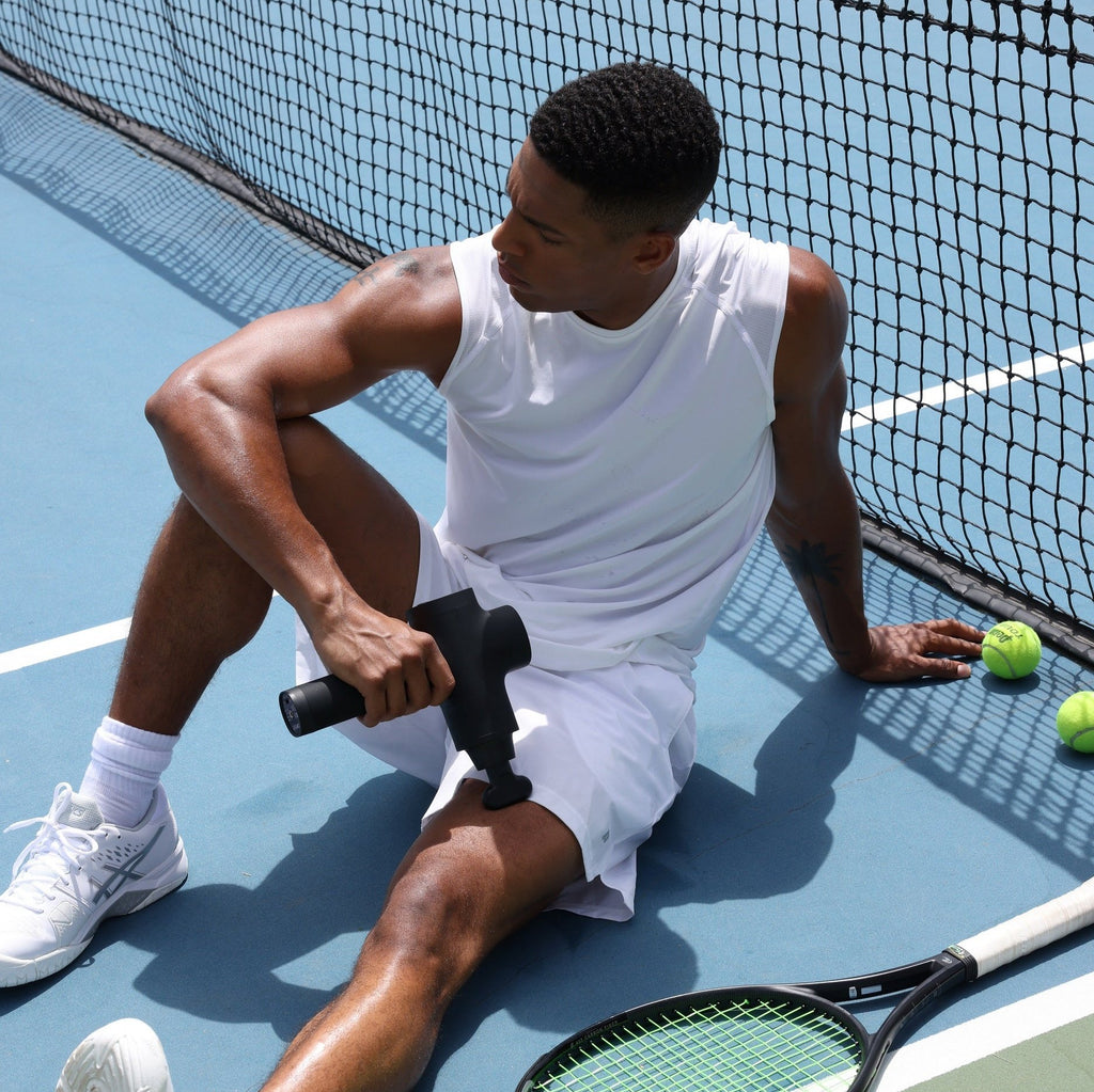 An athlete massages his legs with the Opove M3 Pro massage gun after a tennis match. 