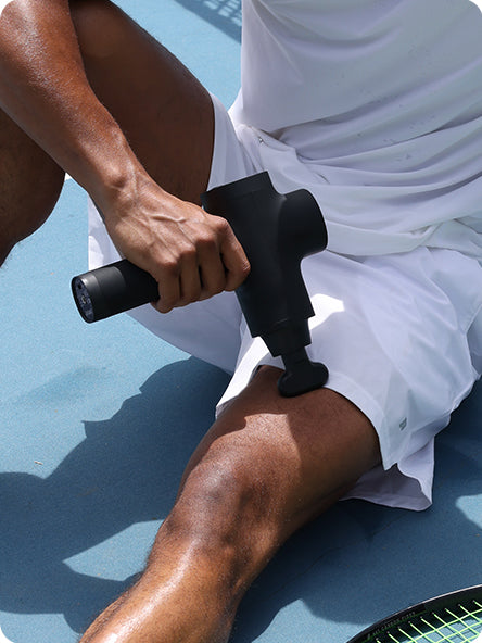 An athlete massages his legs with the Opove M3 Pro massage gun after a tennis match. The professional-grade percussion device delivers deep tissue relief to tired leg muscles